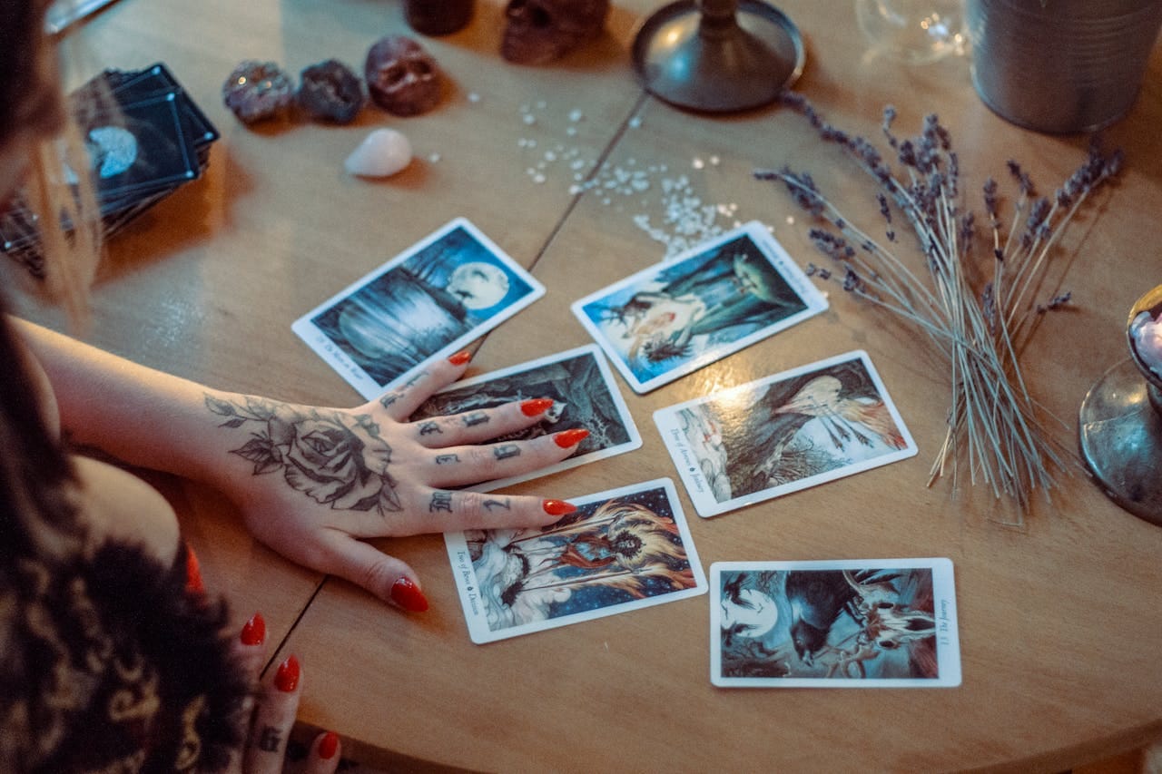 A mystical setup featuring tarot card reading on a wooden table, with artistic tattoos and dried flowers.