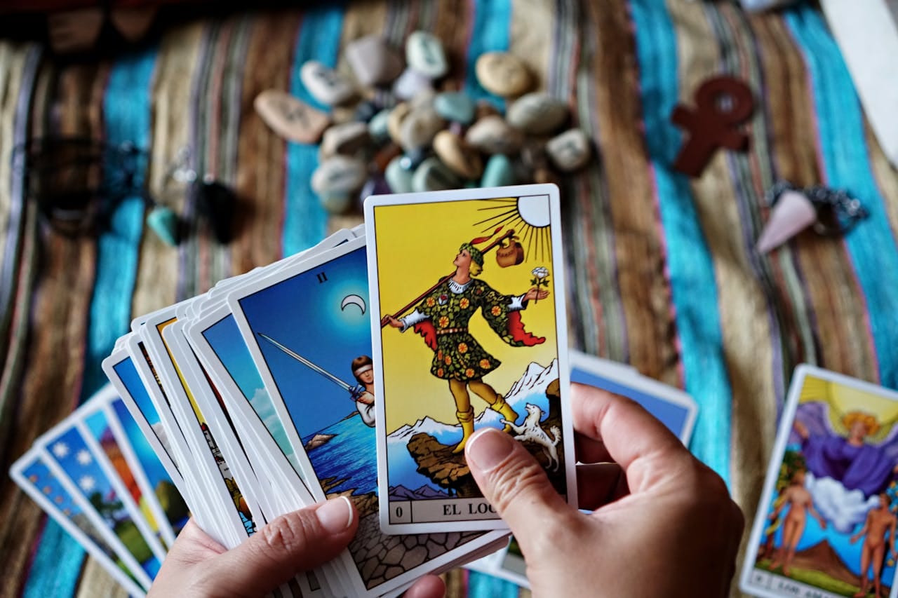 Hands holding tarot cards over a vibrant striped cloth with stones and charms, creating a spiritual atmosphere.